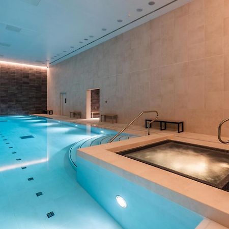 Citysuites 2 Aparthotel Salford  Exterior foto The photo shows an indoor swimming pool area. The pool is a bright blue color and features smooth, tiled surfaces. On one side, there is a hot tub area with steps leading into it. The walls are made of light-colored stone, and there is ambient lighti