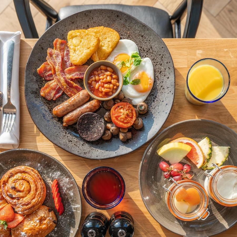 Citysuites 2 Aparthotel Salford  Exterior foto The photo showcases a delicious breakfast spread. On a large, dark plate, there are items including crispy bacon, two fried eggs, baked beans, a grilled tomato, sautéed mushrooms, sausage links, and slices of black pudding. There's also a few pieces 