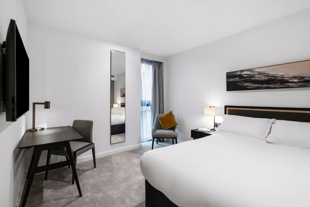 Citysuites 2 Aparthotel Salford  Exterior foto The photo shows a modern hotel room with a clean and minimalist design. It features a large bed with white linens, a small desk with a chair, and a mirror mounted on the wall. There is a chair in one corner with a decorative pillow, and the room has 