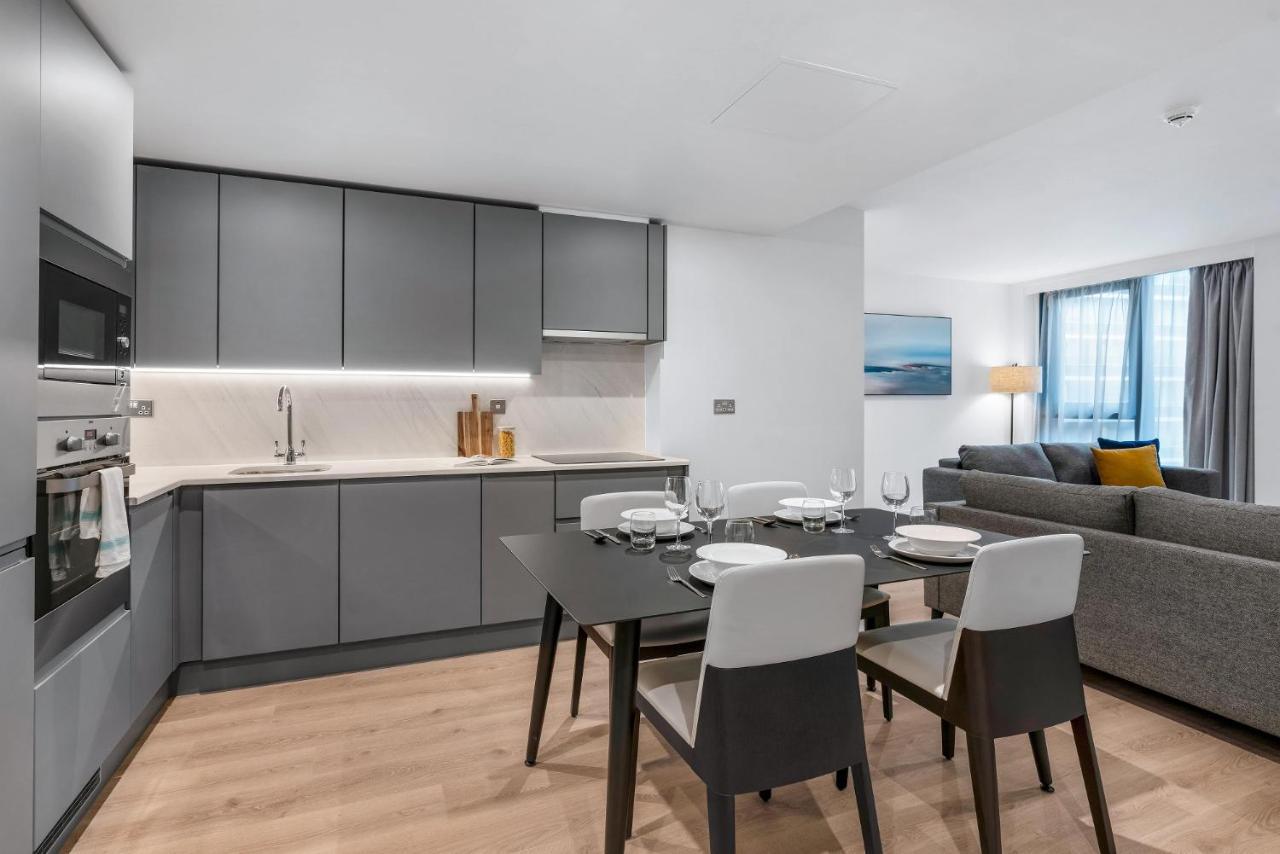 Citysuites 2 Aparthotel Salford  Exterior foto The photo shows a modern, open-concept kitchen and living area. The kitchen features sleek, gray cabinetry with a countertop, a sink, and built-in appliances. There are cooking utensils displayed on the countertop. Next to the kitchen, there is a din