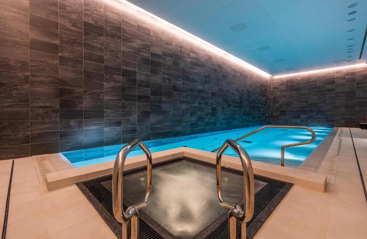 Citysuites 2 Aparthotel Salford  Exterior foto The photo shows a modern indoor swimming pool area. The pool features a sleek, rectangular design with a beautiful blue water that seems illuminated. Surrounding the pool are dark, textured walls, adding to the elegant atmosphere. There are dual meta